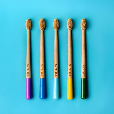 Five SuperBee bamboo toothbrushes in a row, each with a different coloured handle