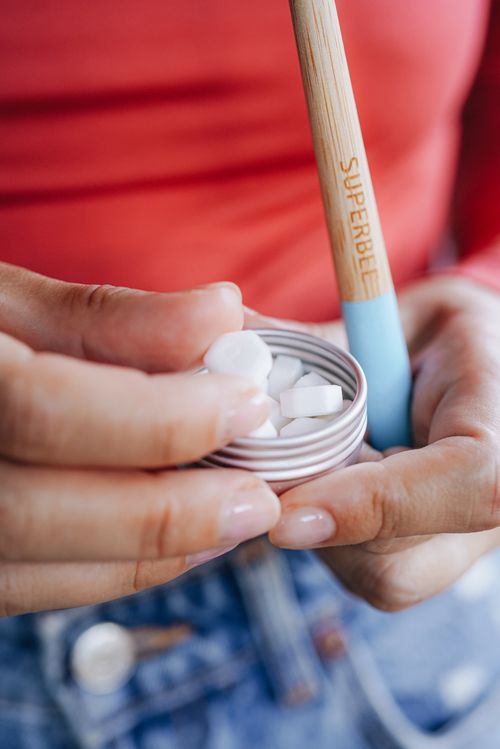 Hands opening a tin of toothpaste tablets with a bamboo toothbrush