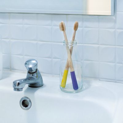 Two SuperBee bamboo toothbrushes standing in a glass beside a bathroom tap