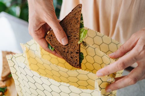 Sliding a rye bread sandwich into a honeycomb-print SuperBee beeswax bag