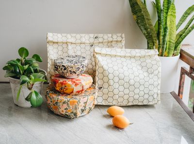 Two SuperBee honeycomb beeswax bags beside bowls covered with beeswax wraps and fresh oranges