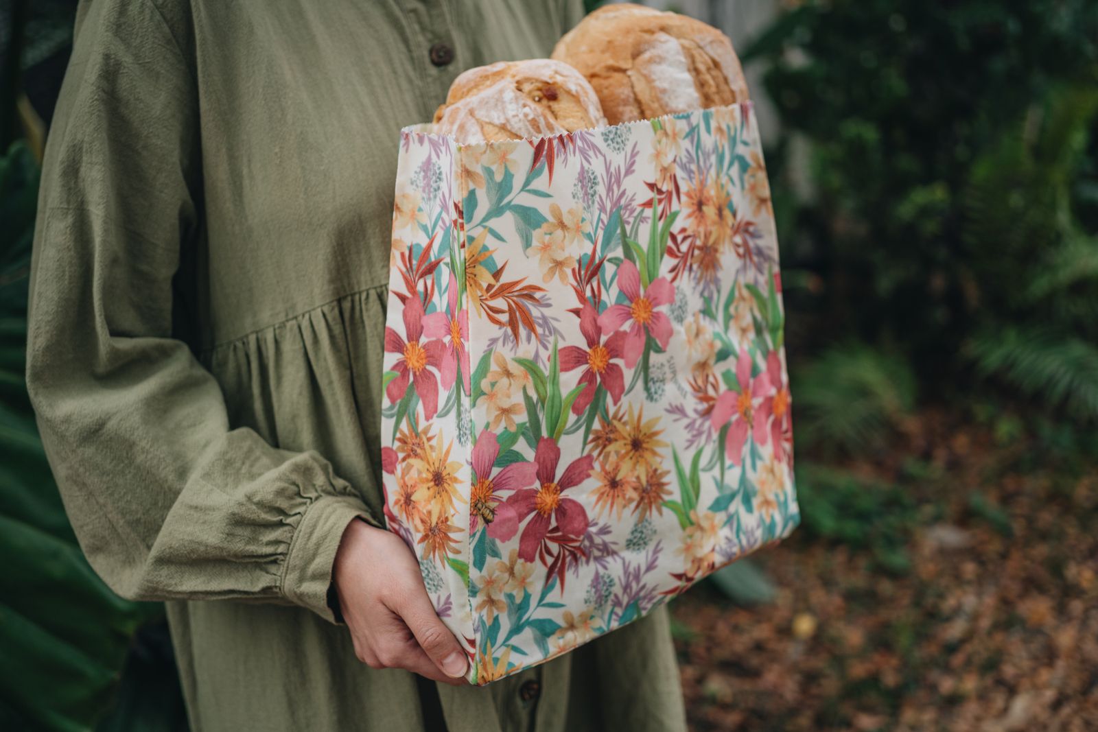 A woman carrying fresh baguettes in a floral SuperBee beeswax bread bag