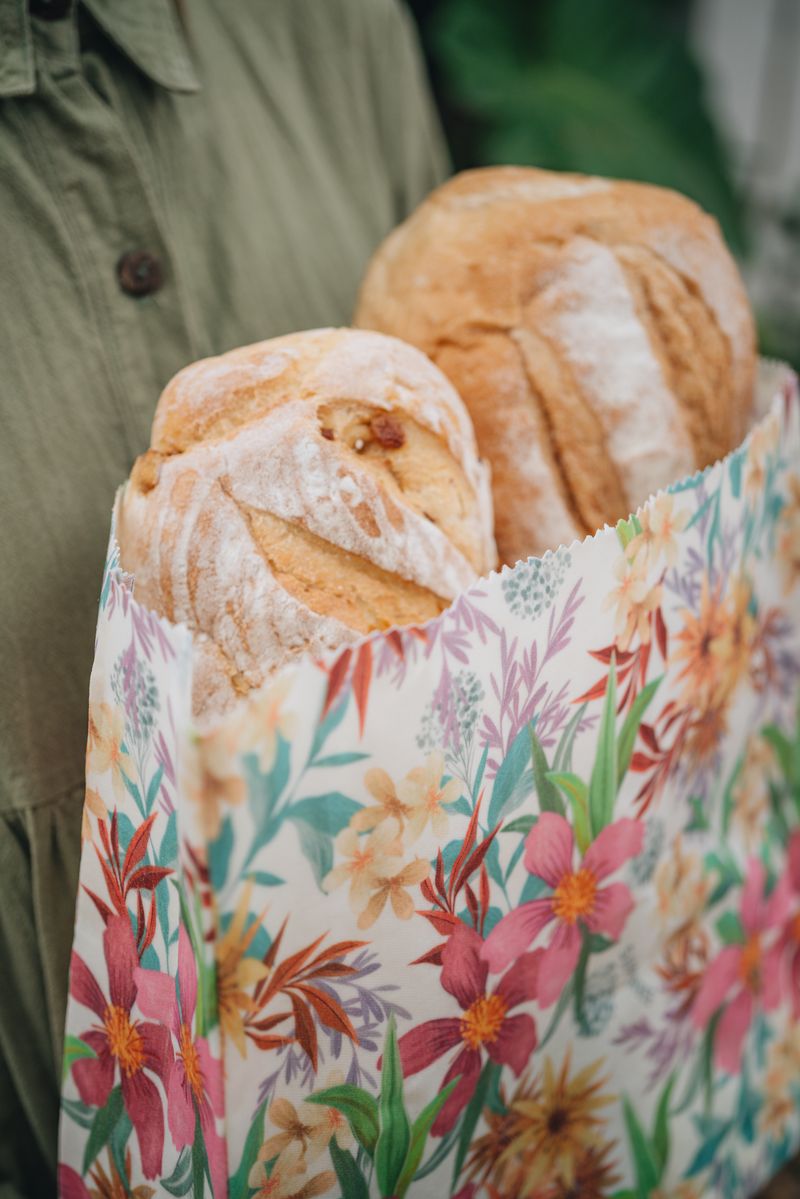 A woman carrying fresh baguettes in a floral SuperBee beeswax bread bag
