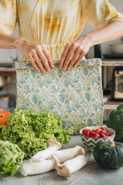 Hands folding a beeswax bag closed over fresh produce