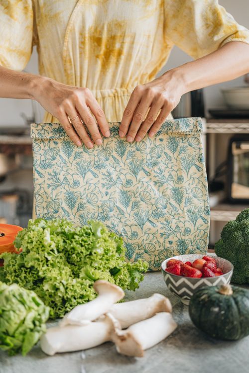 Hands folding closed a large SuperBee beeswax bag on a kitchen counter with lettuce, mushrooms and strawberries