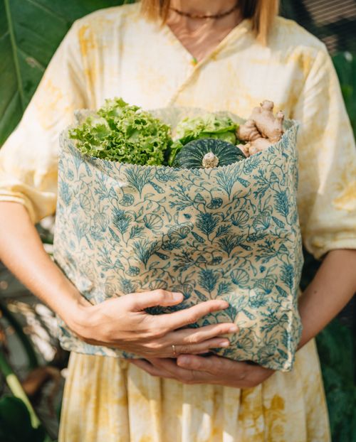 A woman holding a large SuperBee beeswax bag filled with lettuce, a squash and ginger