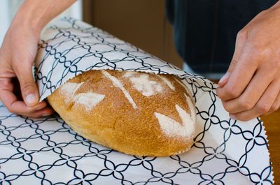 Hands folding a navy geometric beeswax wrap around a sourdough loaf