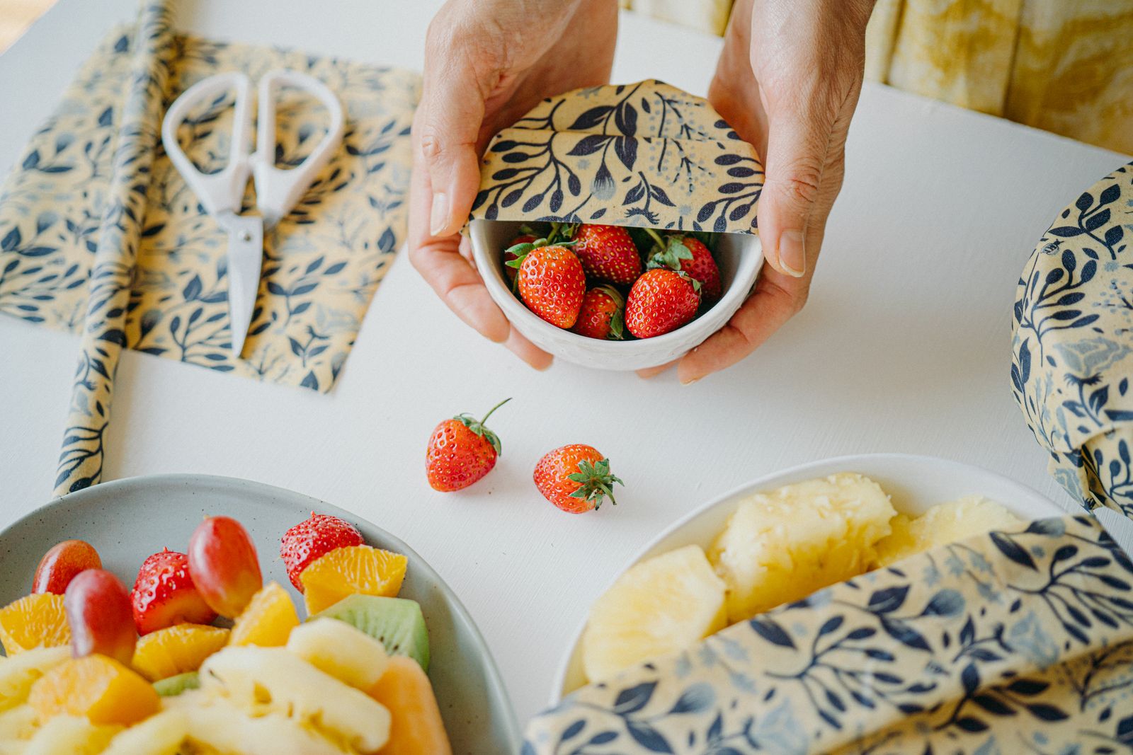 A bowl of strawberries covered with a SuperBee beeswax wrap beside cut fruit