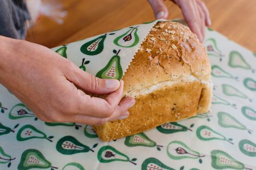 Hands wrapping a loaf of bread in a green pear-print beeswax wrap