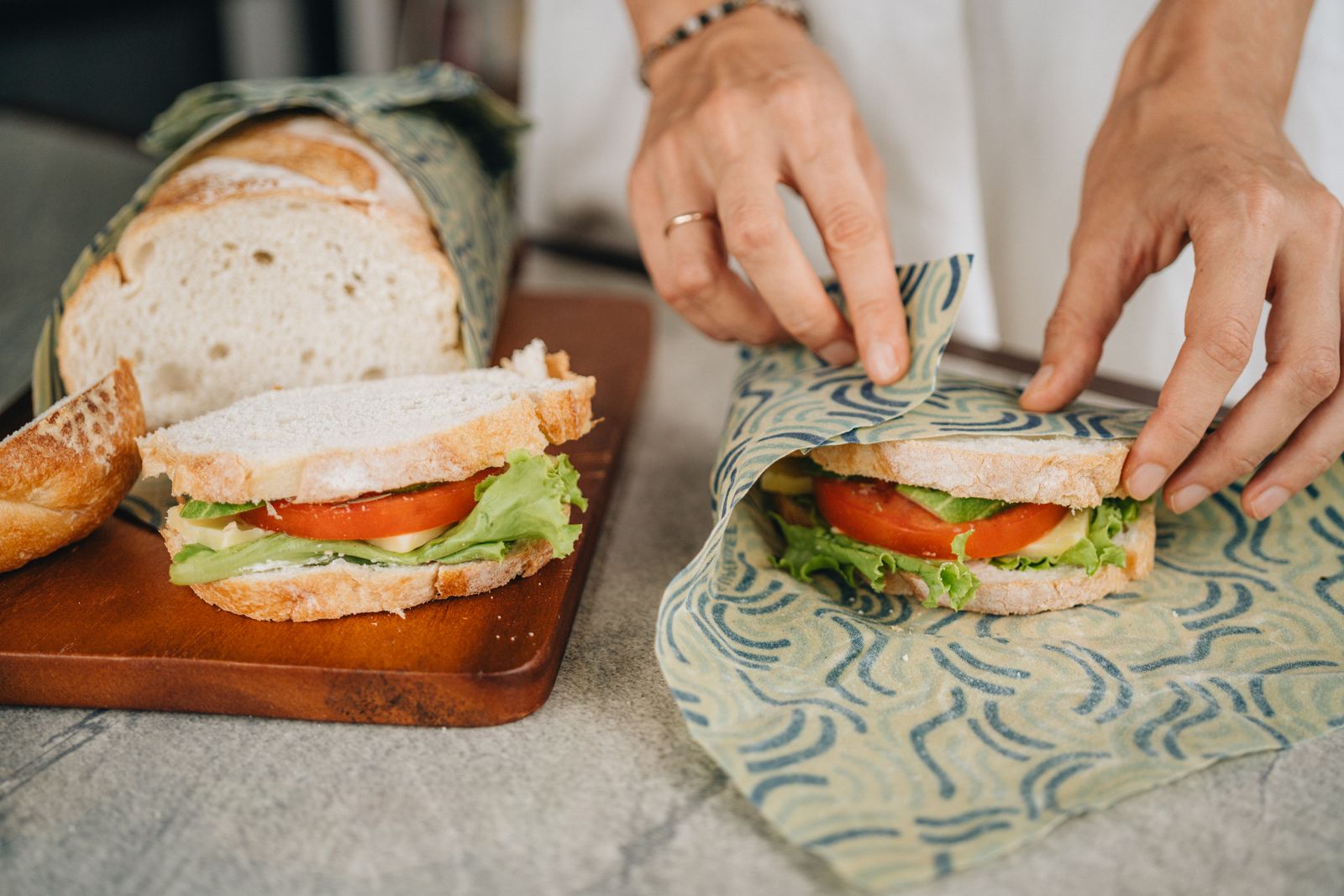 Hands folding a SuperBee beeswax wrap around a fresh sandwich