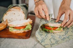 Hands folding a SuperBee beeswax wrap around a fresh sandwich