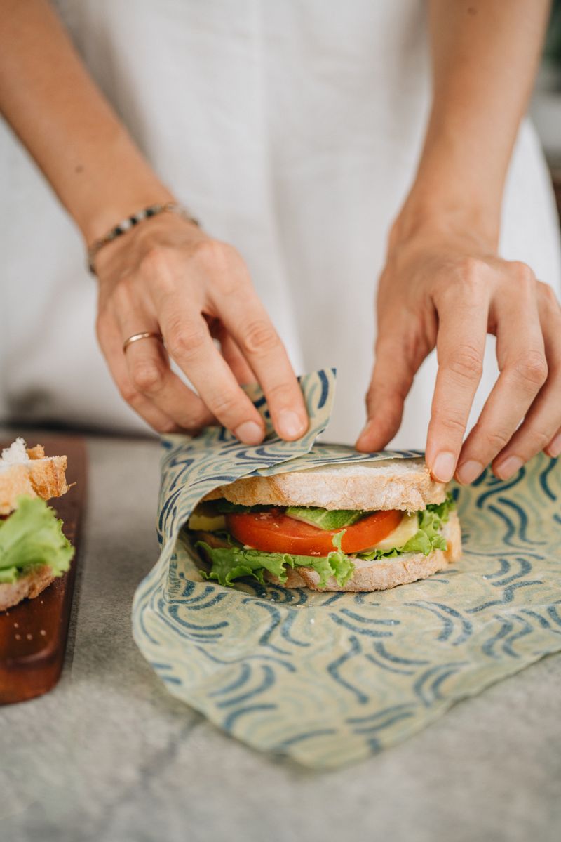 Hands folding a SuperBee beeswax wrap around a fresh sandwich