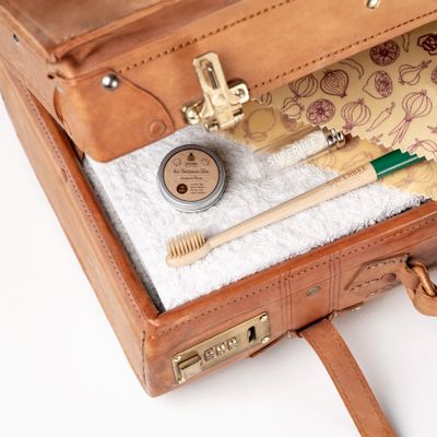 An open vintage suitcase packed with the Dentos oral care travel kit — bamboo toothbrush, tin and floss