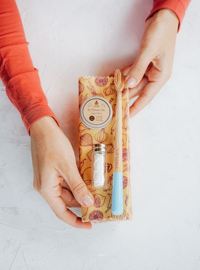 Hands holding the Dentos oral care travel kit in its patterned cotton pouch