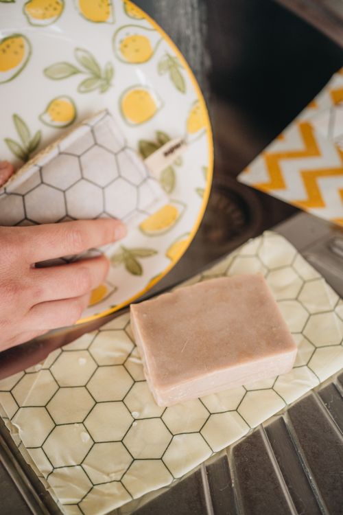 The bare dishwashing soap bar resting on a honeycomb beeswax wrap next to a lemon-print plate