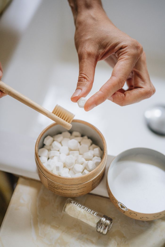 A hand reaching for a Dentos toothpaste tab beside a bamboo toothbrush
