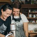Antoinette and a team member laughing together at the waxing table, one with an arm around the other
