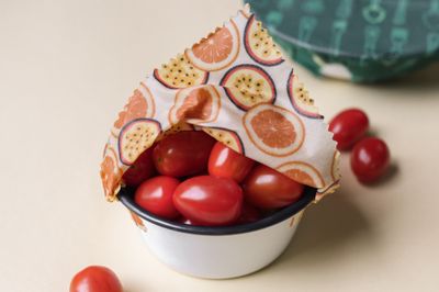 An enamel bowl of cherry tomatoes sealed with an orange-print beeswax wrap