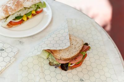 Half a sandwich wrapped in a honeycomb-print beeswax wrap, the other half on a plate