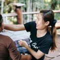 A team member in a flower crown laughing with a colleague at a table on the workshop's veranda