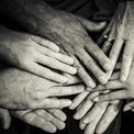Hands of every age stacked together, in black and white