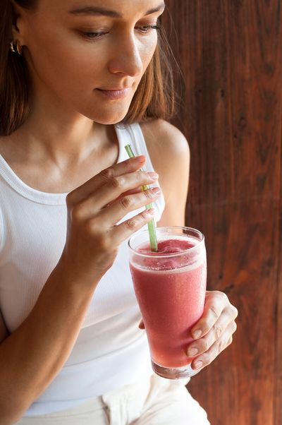 A woman drinking a berry smoothie through a SuperBee glass straw