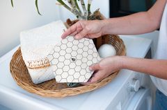 A hand placing a Hexawash laundry sheet into a washing machine of colourful laundry