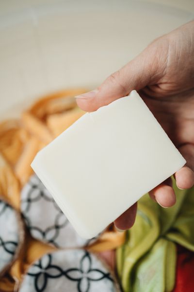 A hand holding the plain white laundry soap bar over a basin of washing