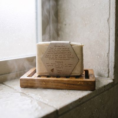 The wrapped laundry soap bar on a wooden soap dish on a steamy windowsill