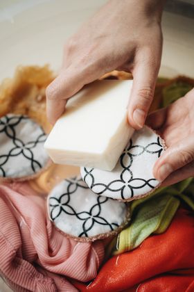 Hands washing SuperBee cotton rounds in a basin with the laundry soap bar