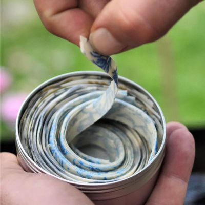 Hands unrolling a SuperBee natural beeswax fire starter from its wax wrap over grass