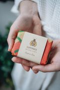 Two hands holding the SuperBee shampoo bar in its printed beeswax wrap and kraft band