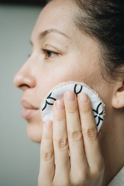 A woman wiping her cheek with a reusable organic cotton round