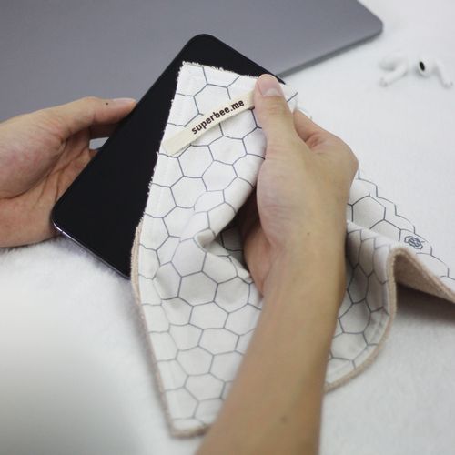 Hands wiping a phone screen with a honeycomb-print SuperBee kitchen cloth