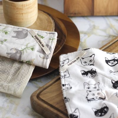 Folded SuperBee reusable kitchen cloths in cat and leaf prints on a wooden board