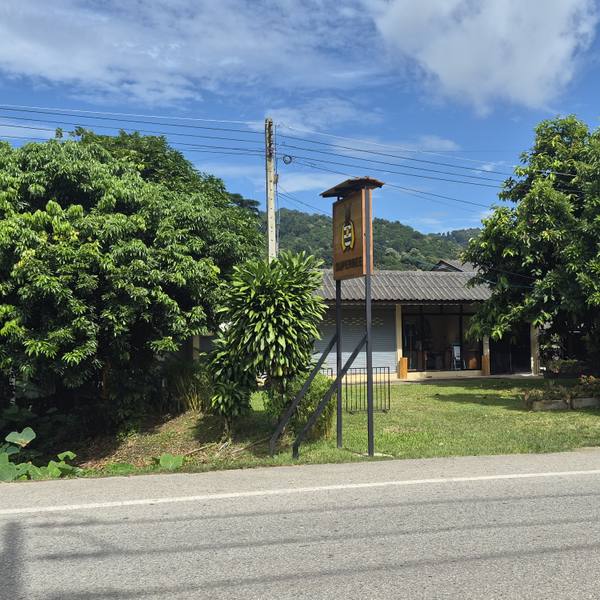 The SuperBee shop and showroom in Mae Ha seen from the road, the sign tower and the hills behind