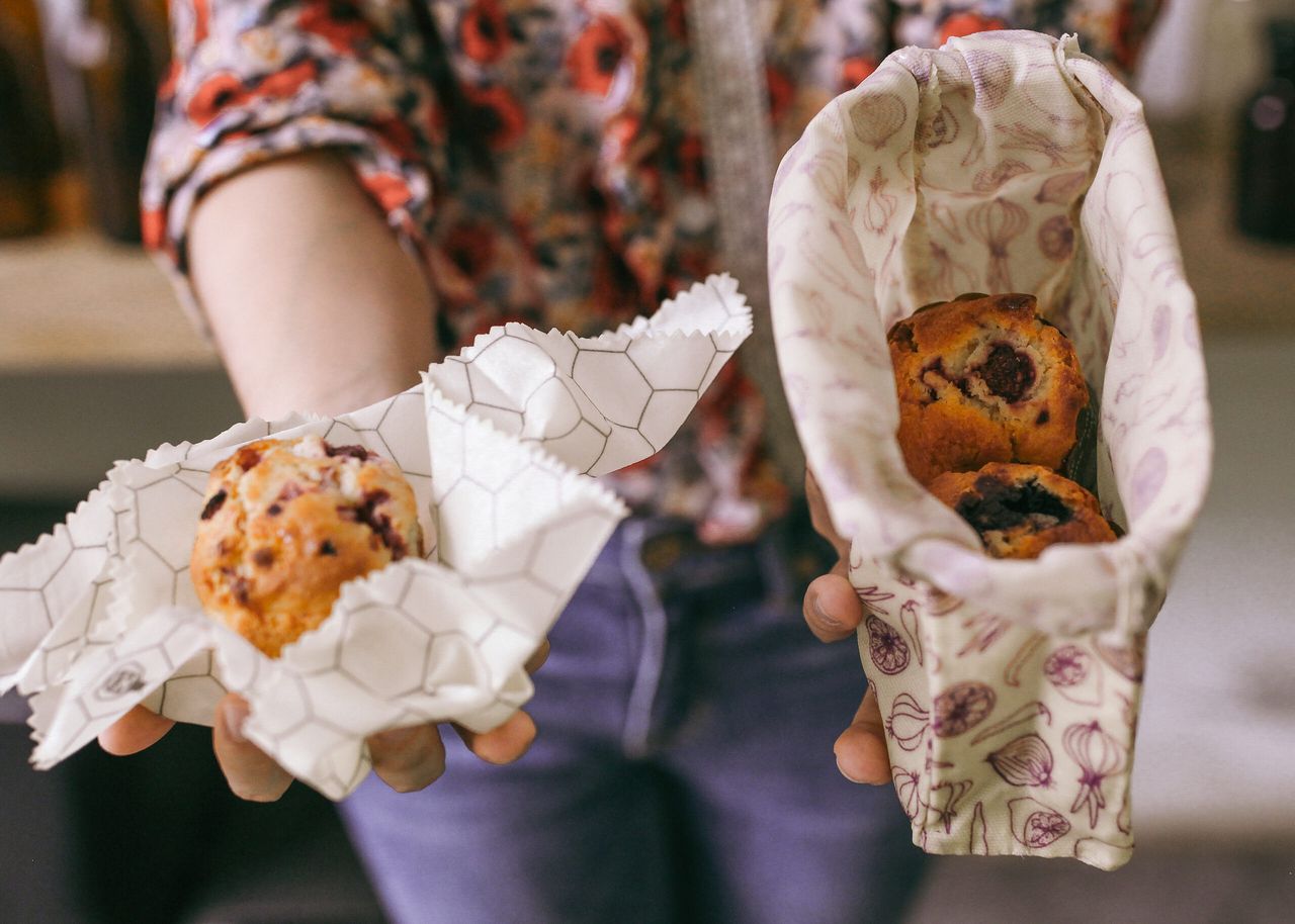 Beeswax wraps and bags holding bread, produce and berries on a kitchen table